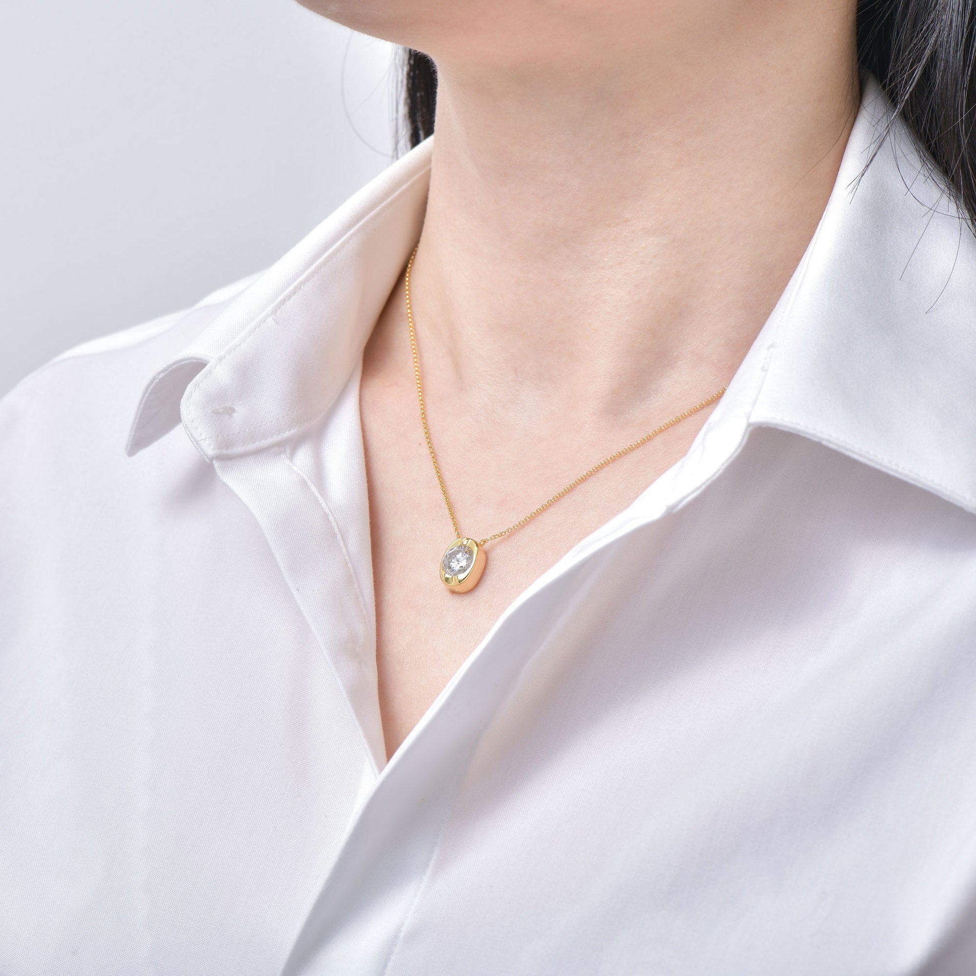 Gold necklace with a pendant worn by a person in a white shirt