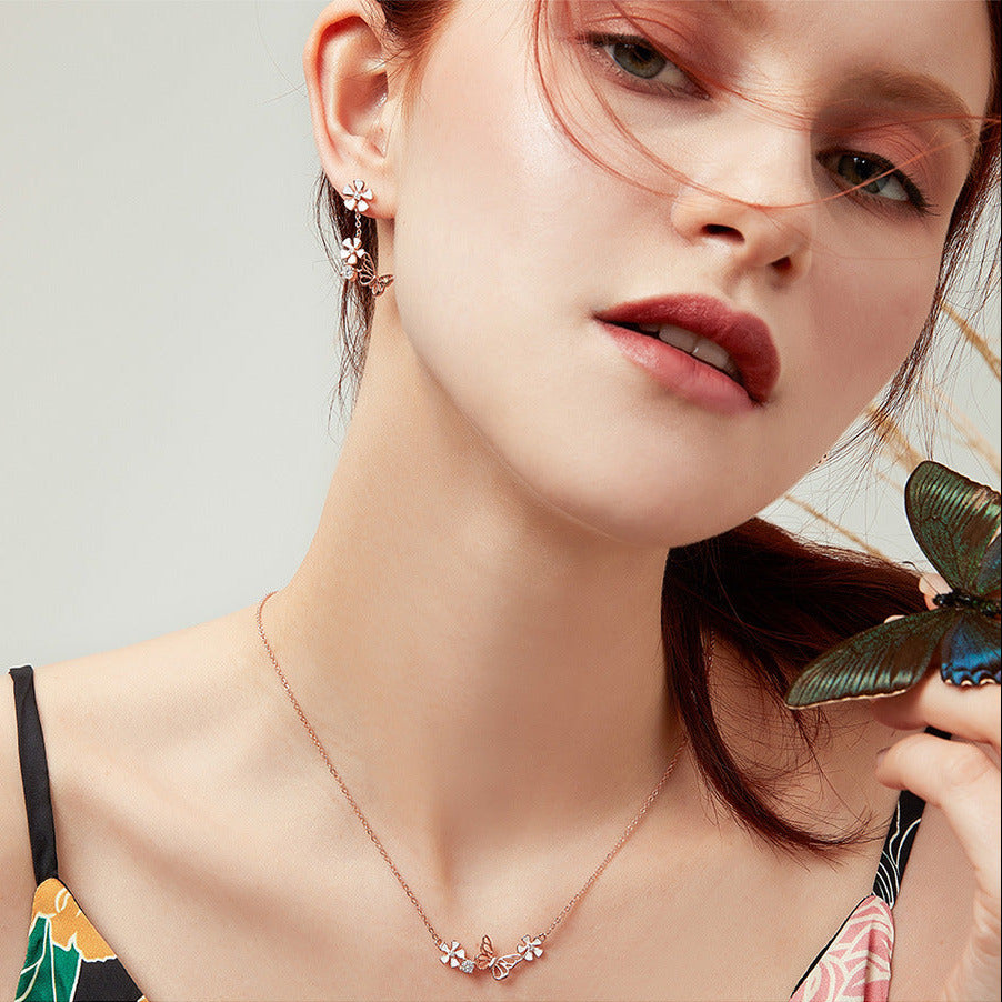 Close-up of a woman wearing a butterfly-themed necklace and earrings with a butterfly in the background.