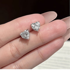 Heart-shaped diamond earrings on a hand with 'BRILLIANT TUN' branding.