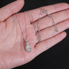 Two silver necklaces with pendants on a hand against a black background