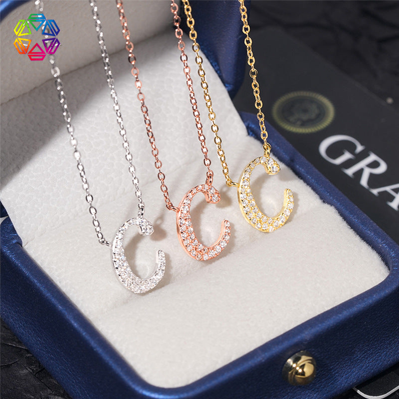 Three necklaces with 'C' pendants in silver, rose gold, and yellow gold on a branded box.