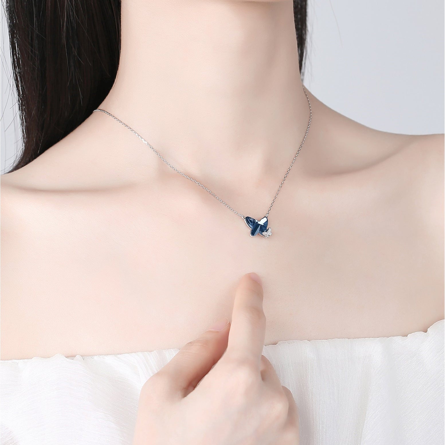 Person wearing a necklace with a butterfly pendant, pointing to it.