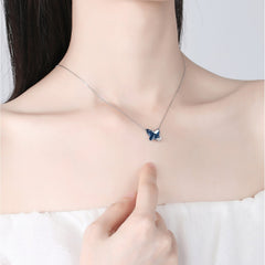 Person wearing a necklace with a butterfly pendant, pointing to it.