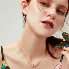 Close-up of a woman wearing a butterfly-themed necklace and earrings with a butterfly in the background.