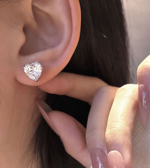 Close-up of a diamond earring being worn on an ear with a hand adjusting it.