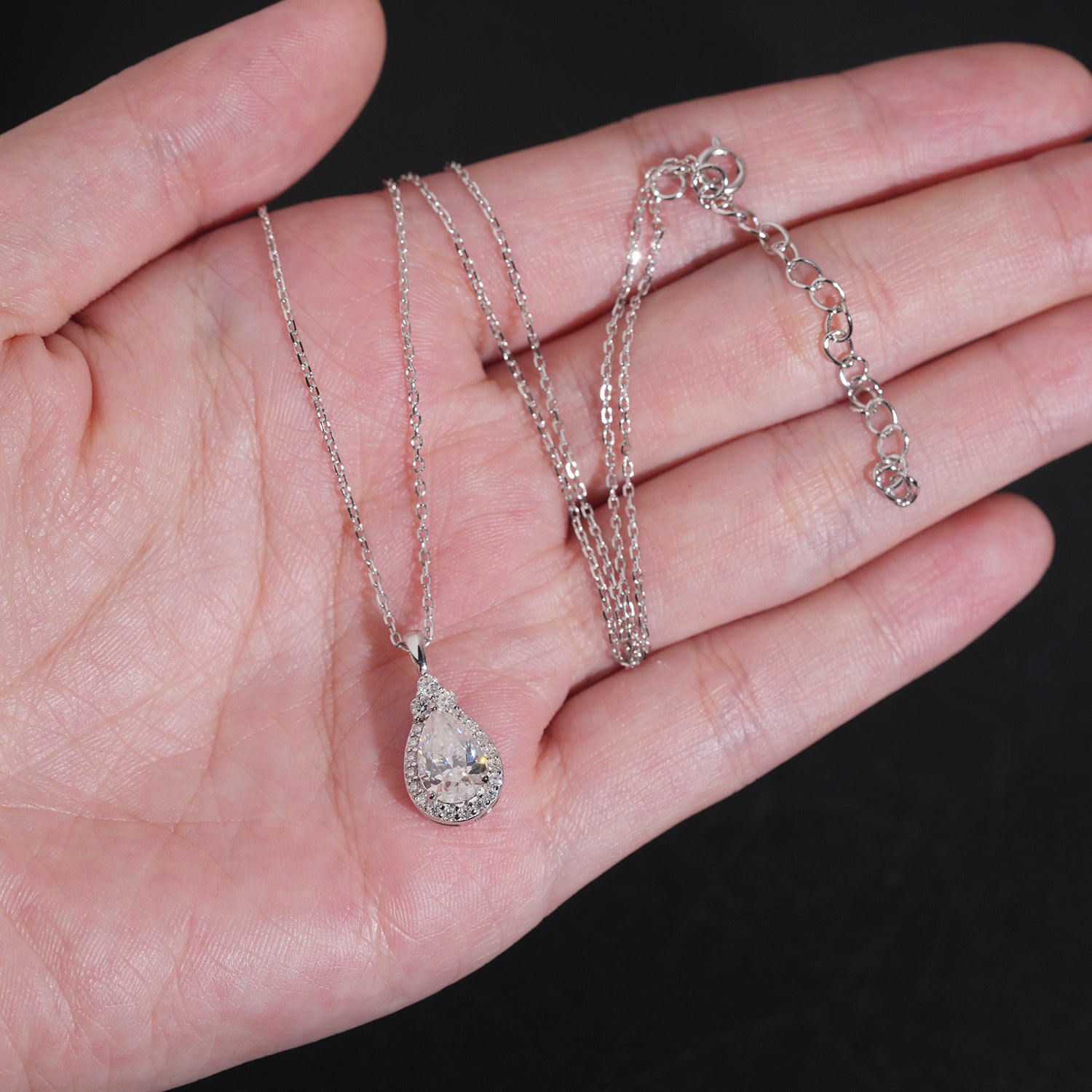 Two silver necklaces with pendants on a hand against a black background
