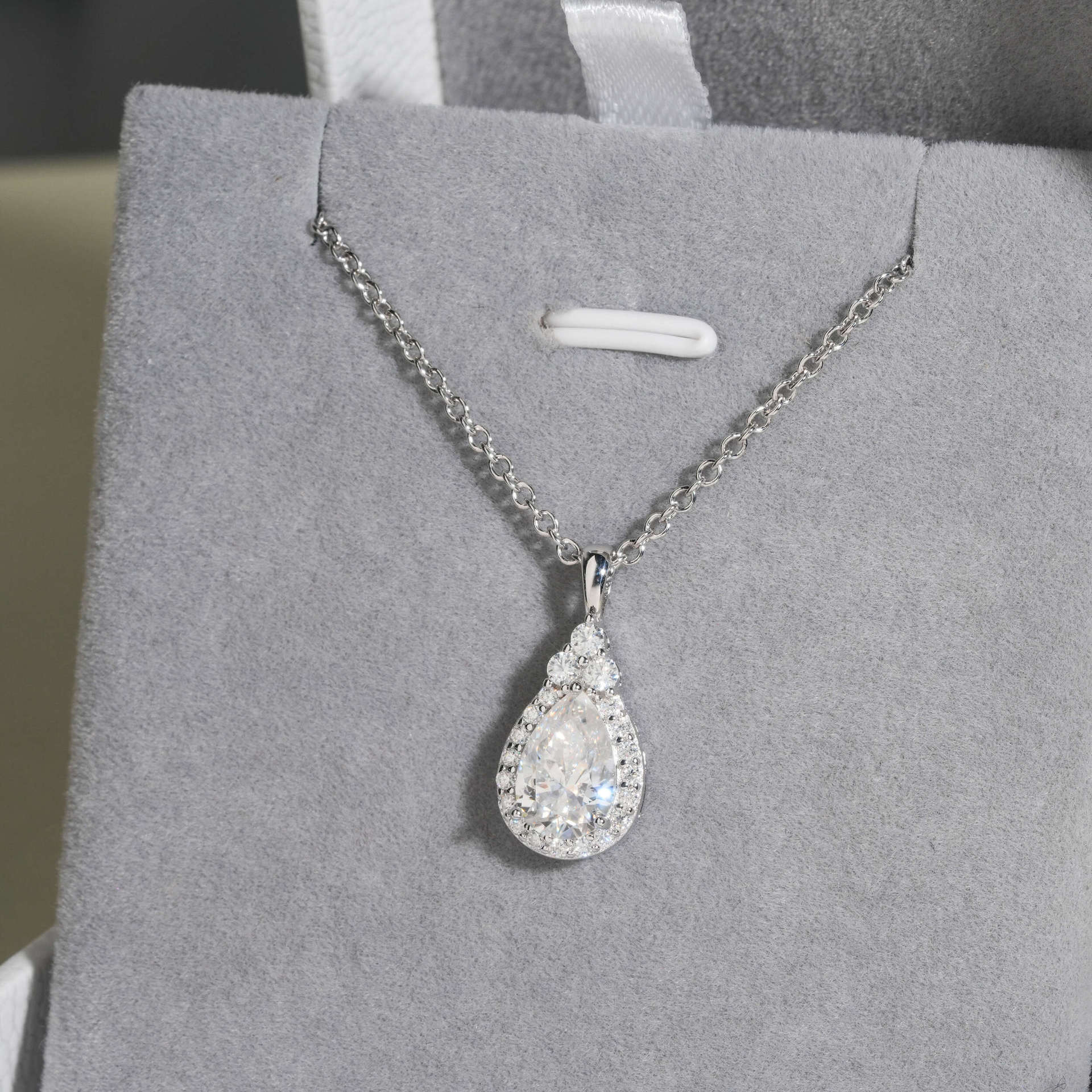 Teardrop-shaped diamond pendant on a chain against a gray background