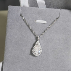 Teardrop-shaped diamond pendant on a chain against a gray background